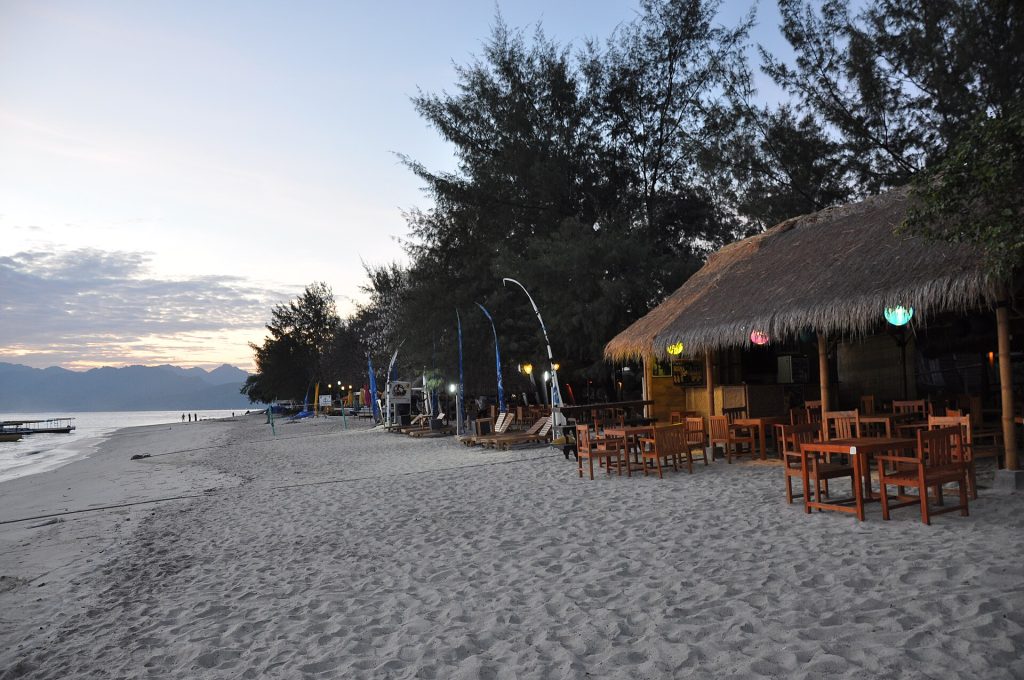 Bar de plage en bois sur le sable de Gili Trawangan, au crépuscule, avec les montagnes de Lombok en arrière-plan