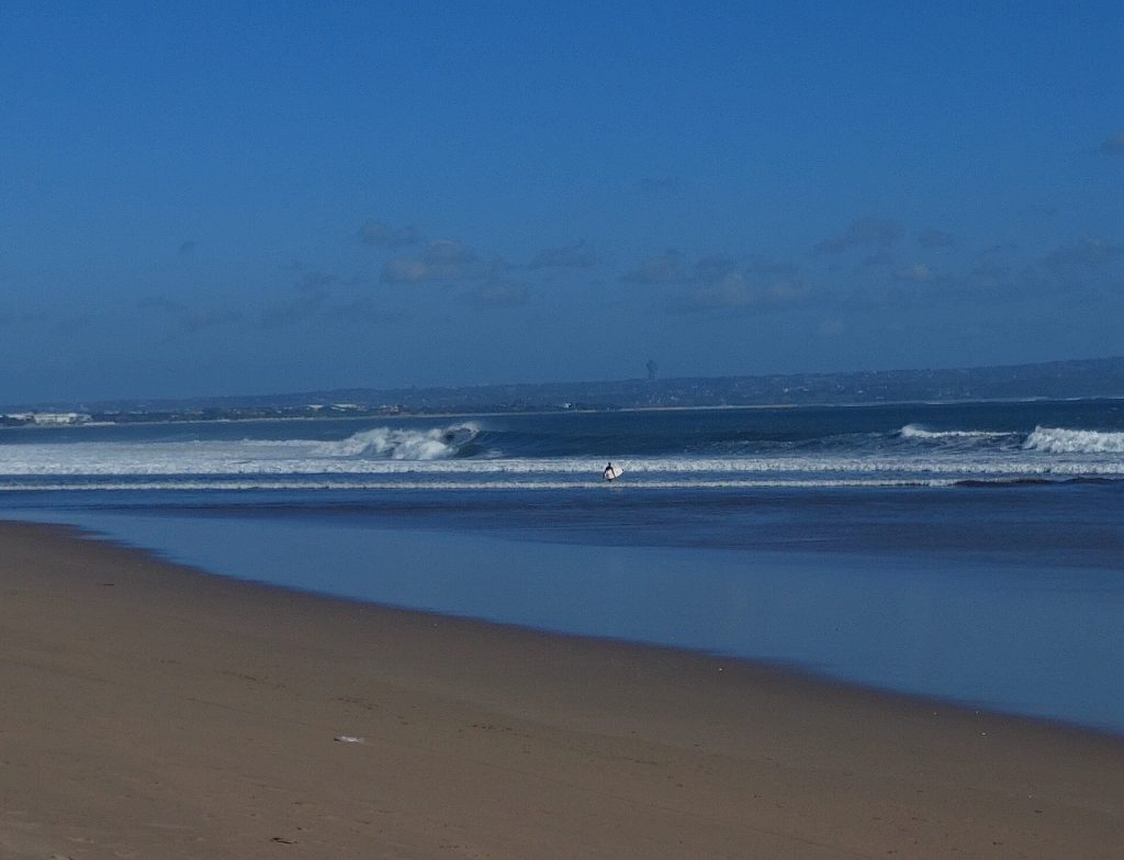 Vagues déferlant sur la plage de Seminyak, avec un surfeur entrant dans l'eau